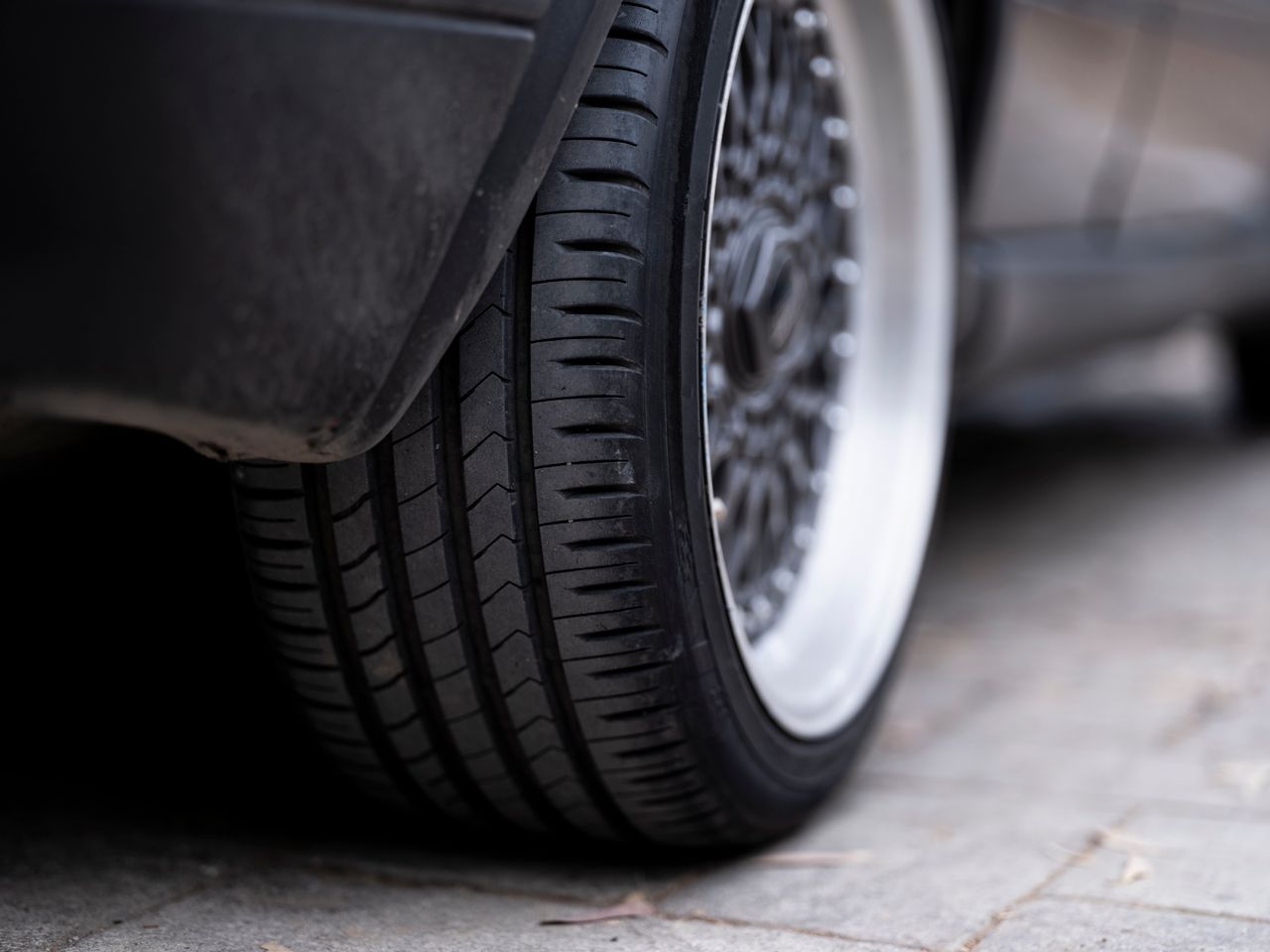 creative-approach-img Detailed view of a car tire on urban pavement, showcasing tread and wheel design.