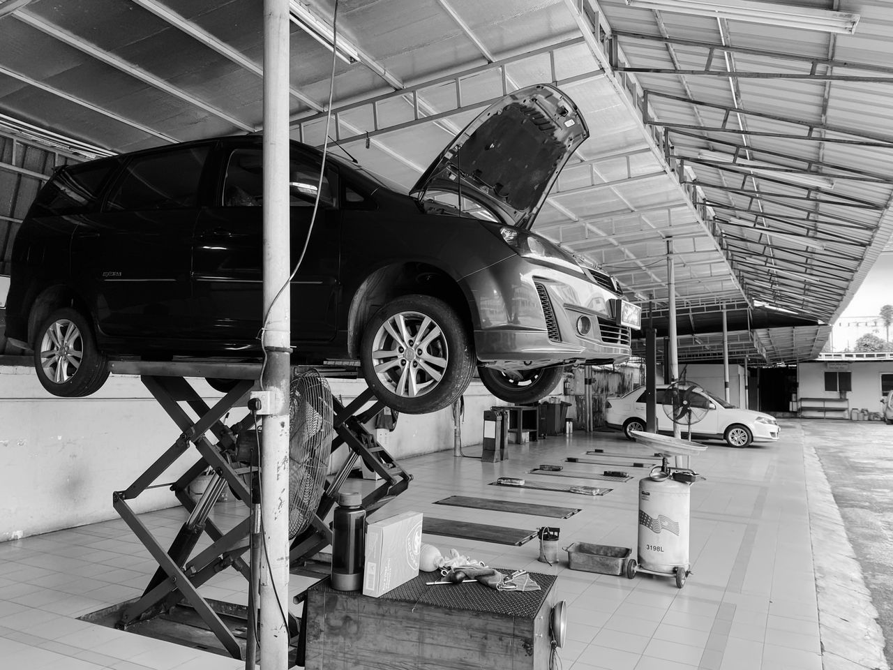 about-img A black and white photo of a vehicle being serviced in a workshop in Ipoh, Malaysia.